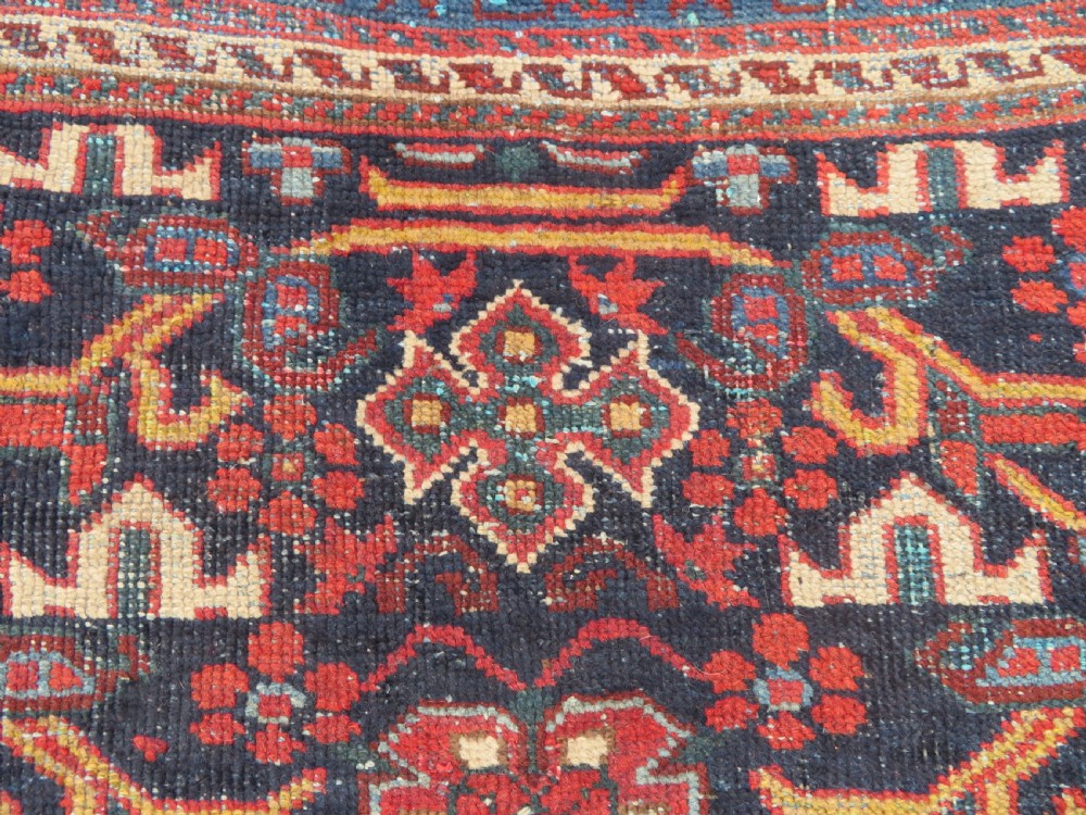 A rectangular hand-knotted antique Afshar rug featuring geometric floral motifs in terracotta red and sky blue on a deep navy blue background. View VI