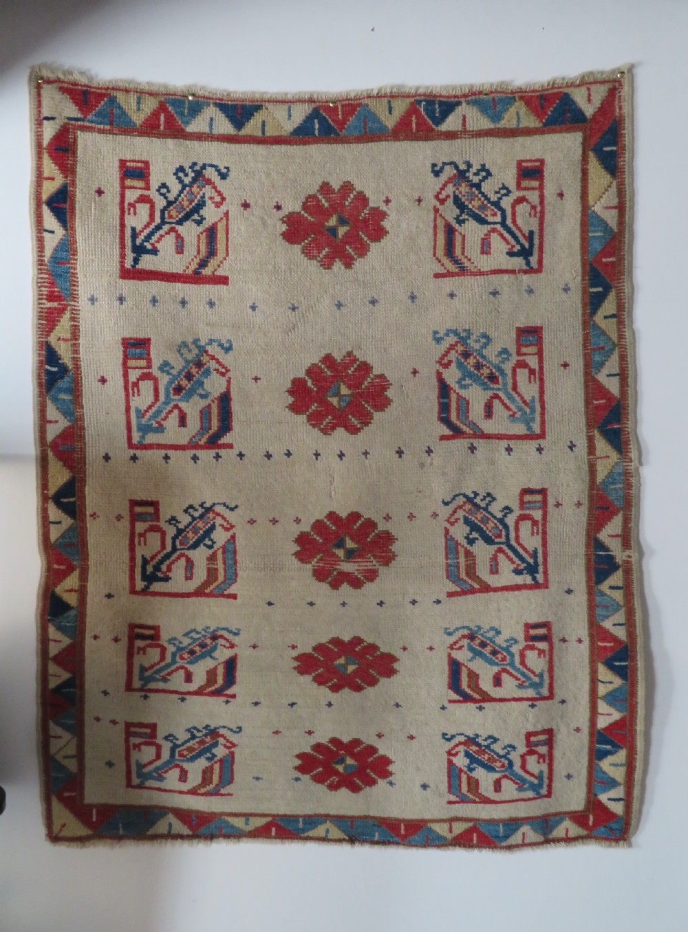 An antique Anatolian Konya wool rug featuring geometric red and blue symbols on a cream field with a sawtooth border.