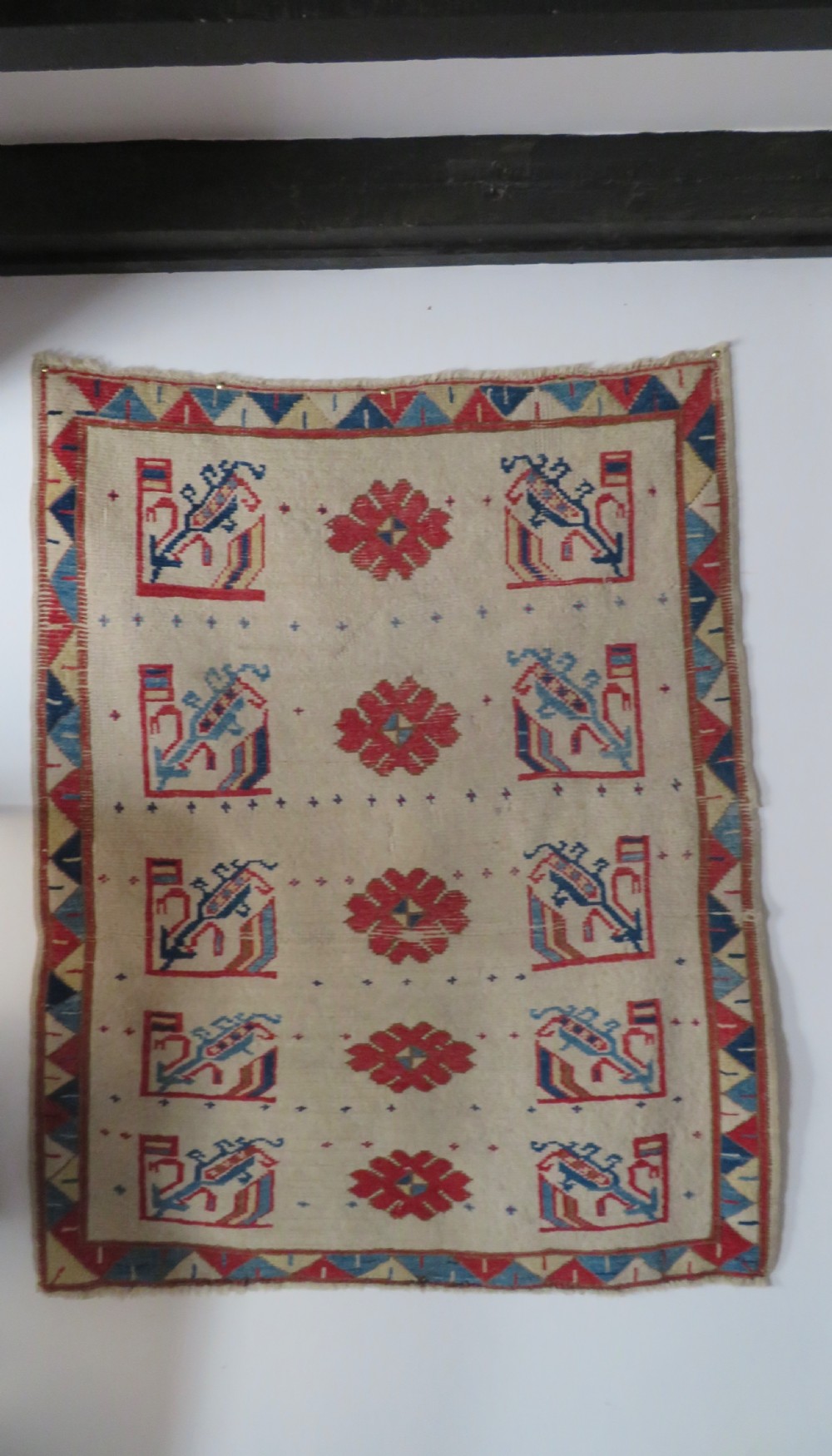 An antique Anatolian Konya wool rug featuring geometric red and blue symbols on a cream field with a sawtooth border. View II