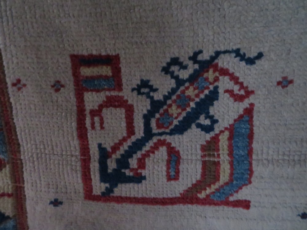 An antique Anatolian Konya wool rug featuring geometric red and blue symbols on a cream field with a sawtooth border. View III
