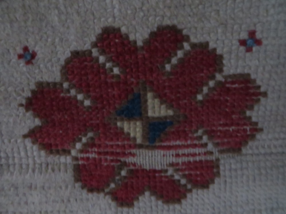 An antique Anatolian Konya wool rug featuring geometric red and blue symbols on a cream field with a sawtooth border. View V