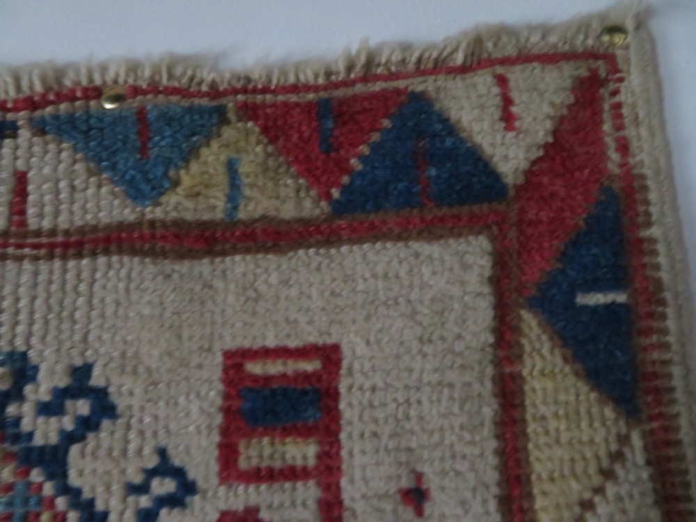 An antique Anatolian Konya wool rug featuring geometric red and blue symbols on a cream field with a sawtooth border. View VII