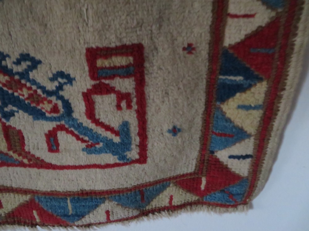An antique Anatolian Konya wool rug featuring geometric red and blue symbols on a cream field with a sawtooth border. View XI