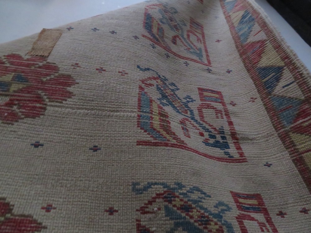 An antique Anatolian Konya wool rug featuring geometric red and blue symbols on a cream field with a sawtooth border. View XII