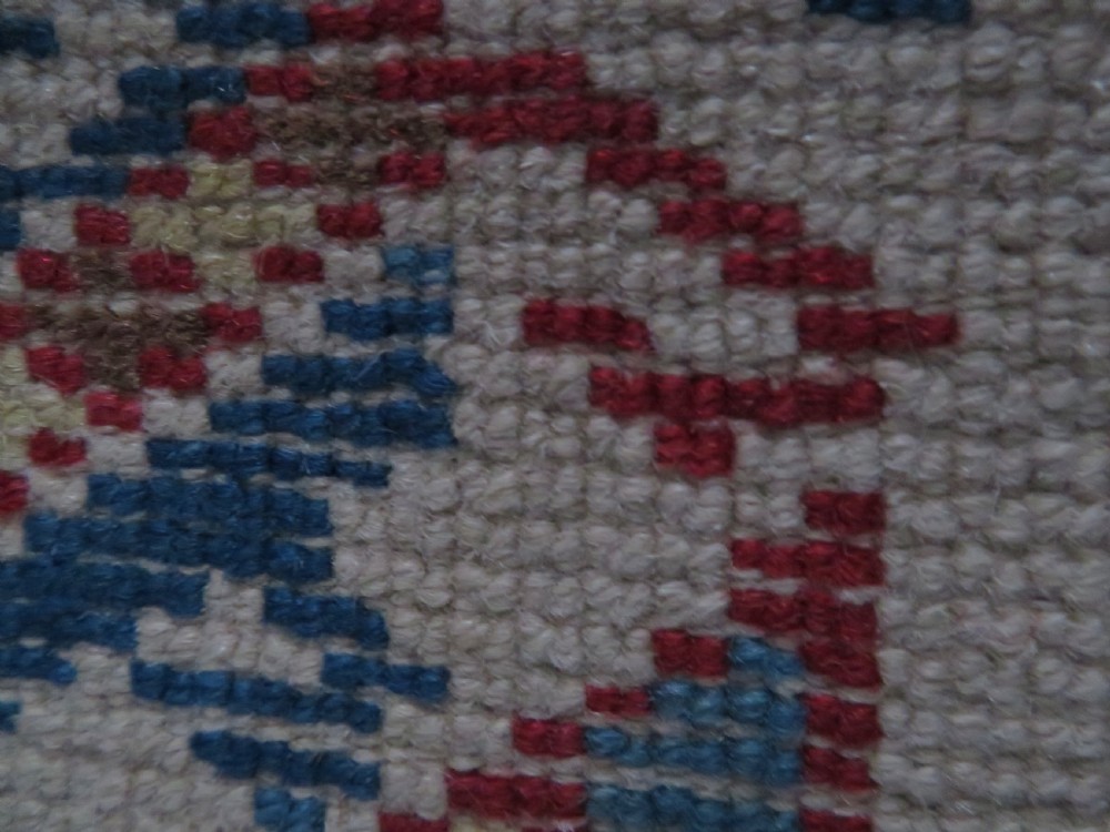 An antique Anatolian Konya wool rug featuring geometric red and blue symbols on a cream field with a sawtooth border. View XIV