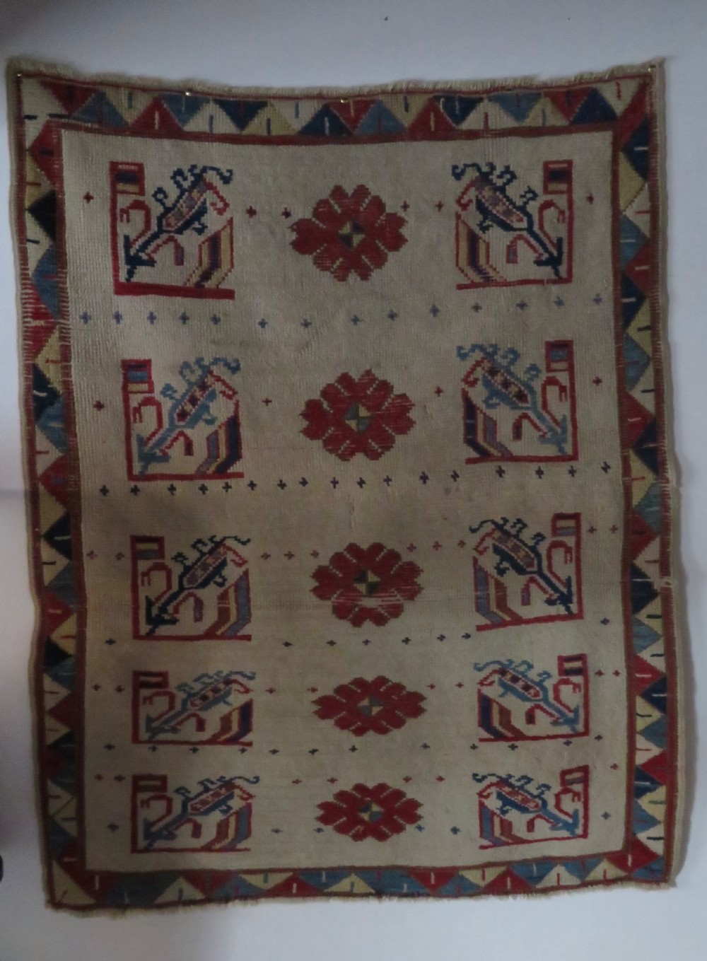 An antique Anatolian Konya wool rug featuring geometric red and blue symbols on a cream field with a sawtooth border. View XV