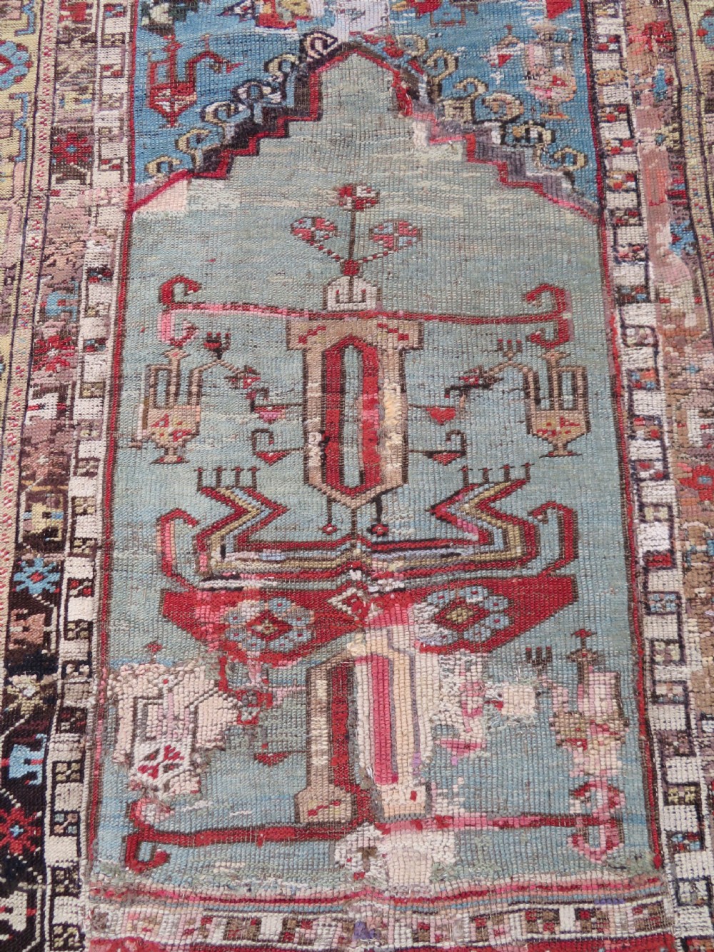 An antique hand-knotted Turkish Ladik wool prayer rug featuring a central pale blue mihrab niche, inverted tulip motifs, and multi-coloured geometric borders. View II
