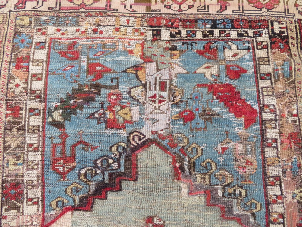 An antique hand-knotted Turkish Ladik wool prayer rug featuring a central pale blue mihrab niche, inverted tulip motifs, and multi-coloured geometric borders. View IV