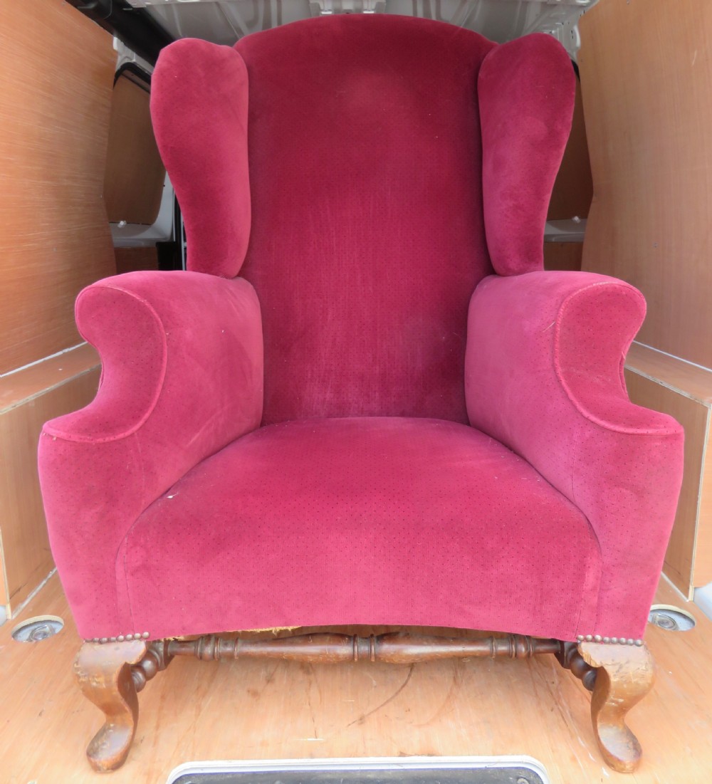 An antique wingback armchair upholstered in crimson velvet with turned wooden stretchers and cabriole front legs.