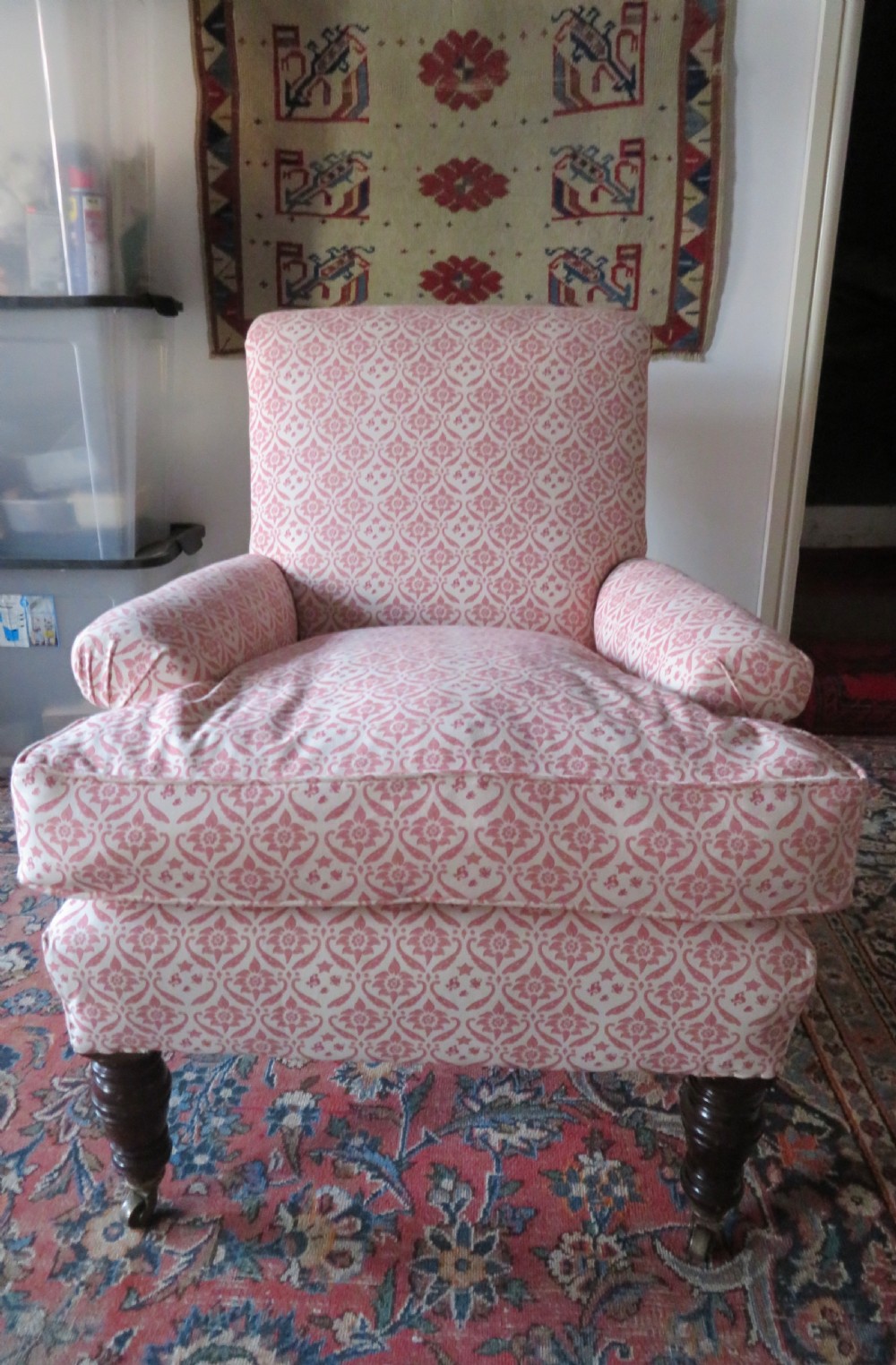 An upholstered Victorian armchair featuring patterned pink and cream fabric, turned dark timber legs, and brass castors.