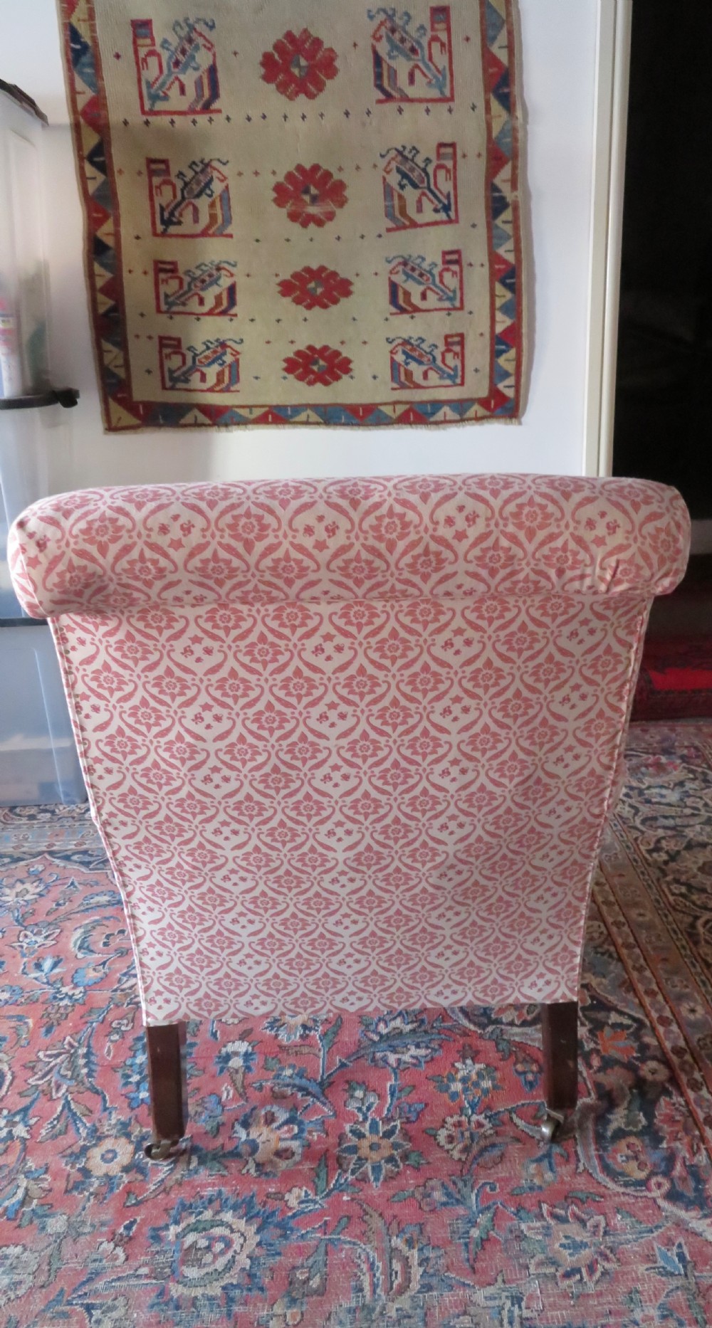 An upholstered Victorian armchair featuring patterned pink and cream fabric, turned dark timber legs, and brass castors. View VI