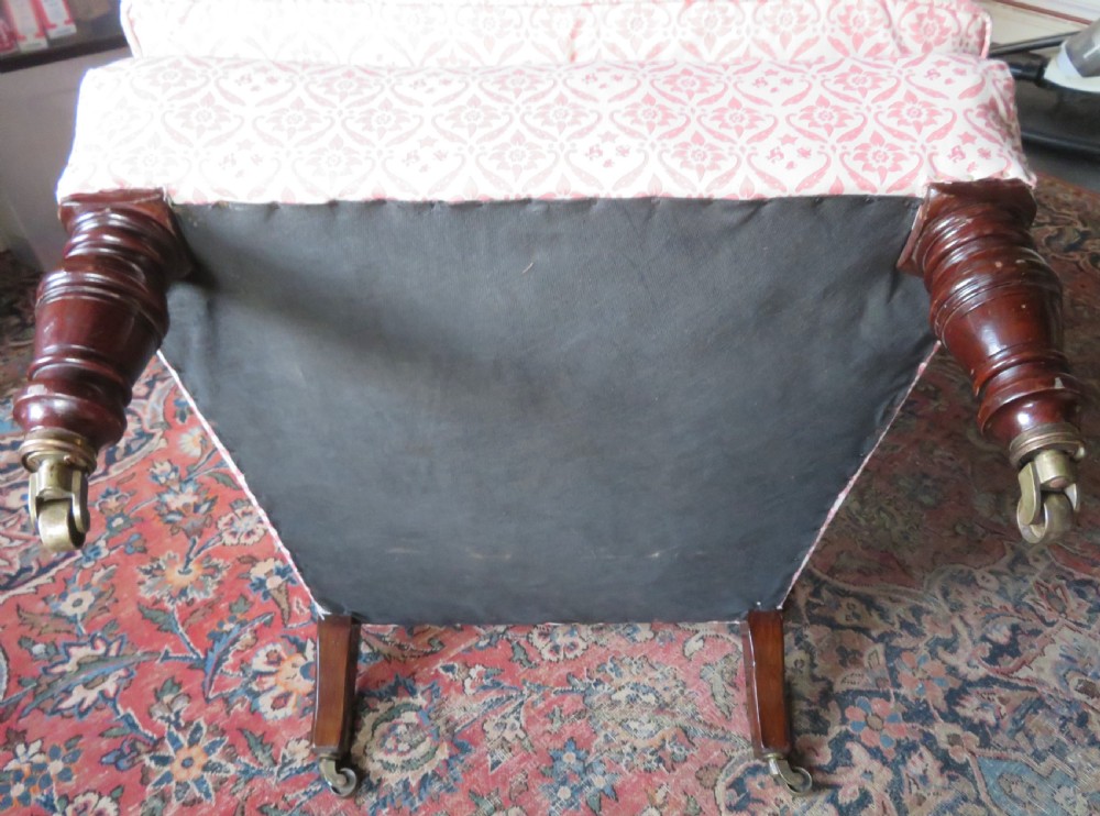 An upholstered Victorian armchair featuring patterned pink and cream fabric, turned dark timber legs, and brass castors. View VIII