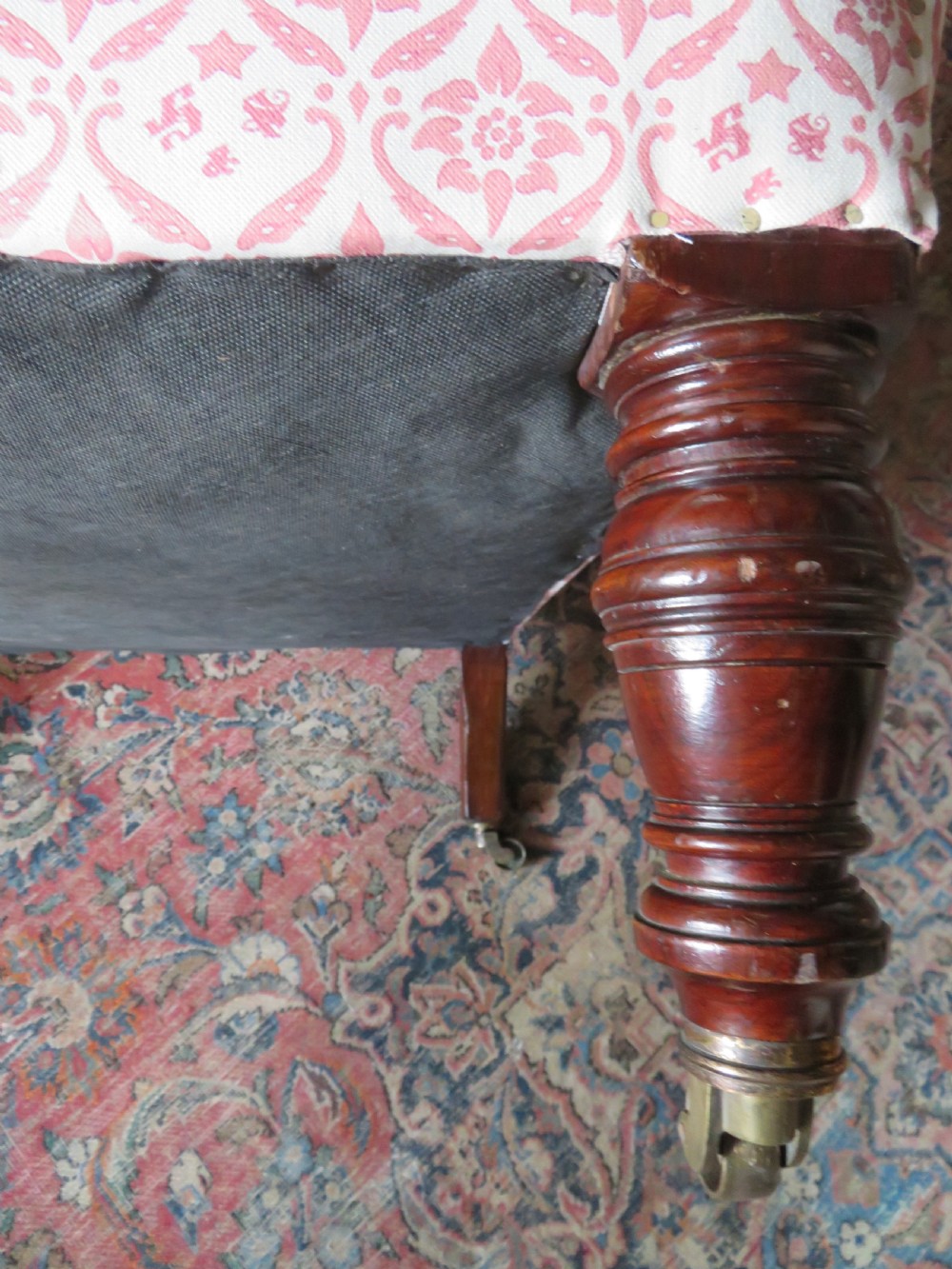An upholstered Victorian armchair featuring patterned pink and cream fabric, turned dark timber legs, and brass castors. View IX