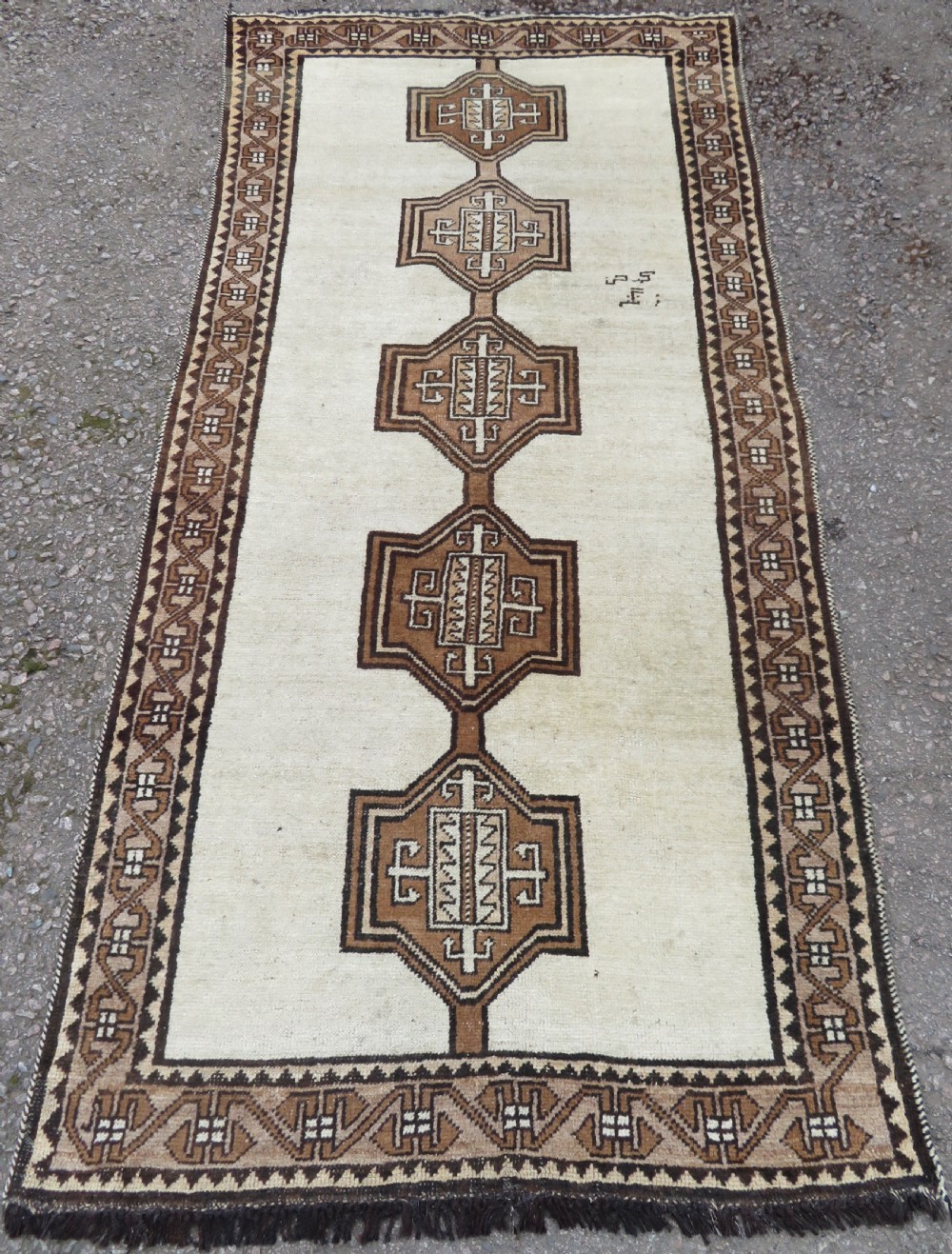 An antique hand-knotted wool Gabbeh rug with five central geometric diamond medallions in brown set against a cream field with a detailed geometric border.