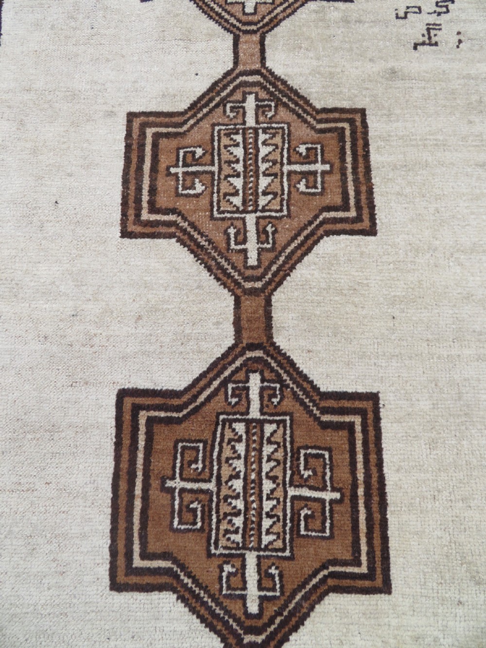 An antique hand-knotted wool Gabbeh rug with five central geometric diamond medallions in brown set against a cream field with a detailed geometric border. View II