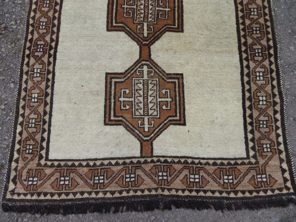 An antique hand-knotted wool Gabbeh rug with five central geometric diamond medallions in brown set against a cream field with a detailed geometric border. View III