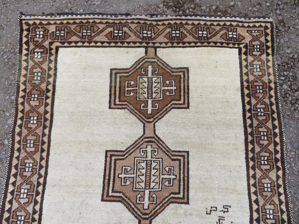 An antique hand-knotted wool Gabbeh rug with five central geometric diamond medallions in brown set against a cream field with a detailed geometric border. View IV