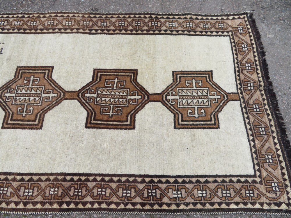An antique hand-knotted wool Gabbeh rug with five central geometric diamond medallions in brown set against a cream field with a detailed geometric border. View VIII