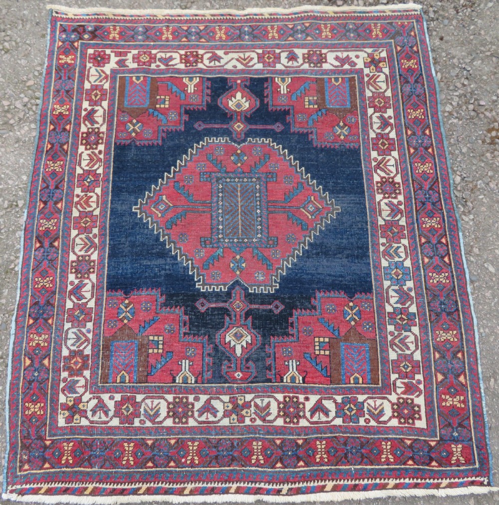 A hand-knotted antique Afshar tribal wool rug featuring a red stepped medallion on an indigo blue field surrounded by geometric borders.