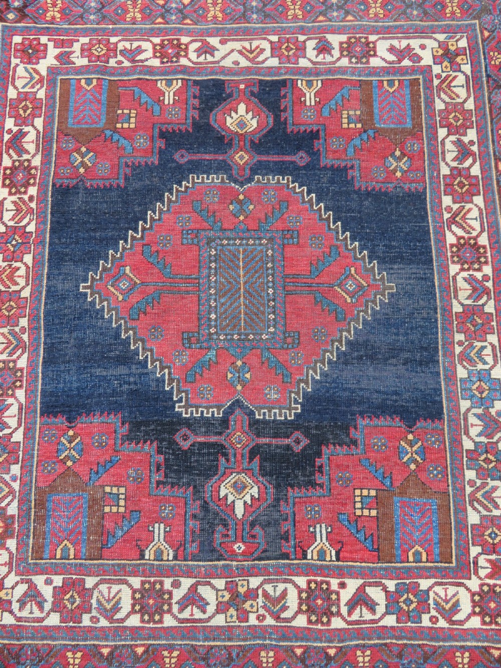 A hand-knotted antique Afshar tribal wool rug featuring a red stepped medallion on an indigo blue field surrounded by geometric borders. View II