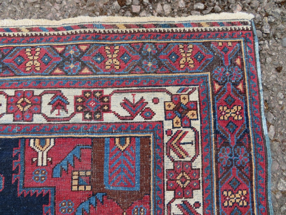 A hand-knotted antique Afshar tribal wool rug featuring a red stepped medallion on an indigo blue field surrounded by geometric borders. View V