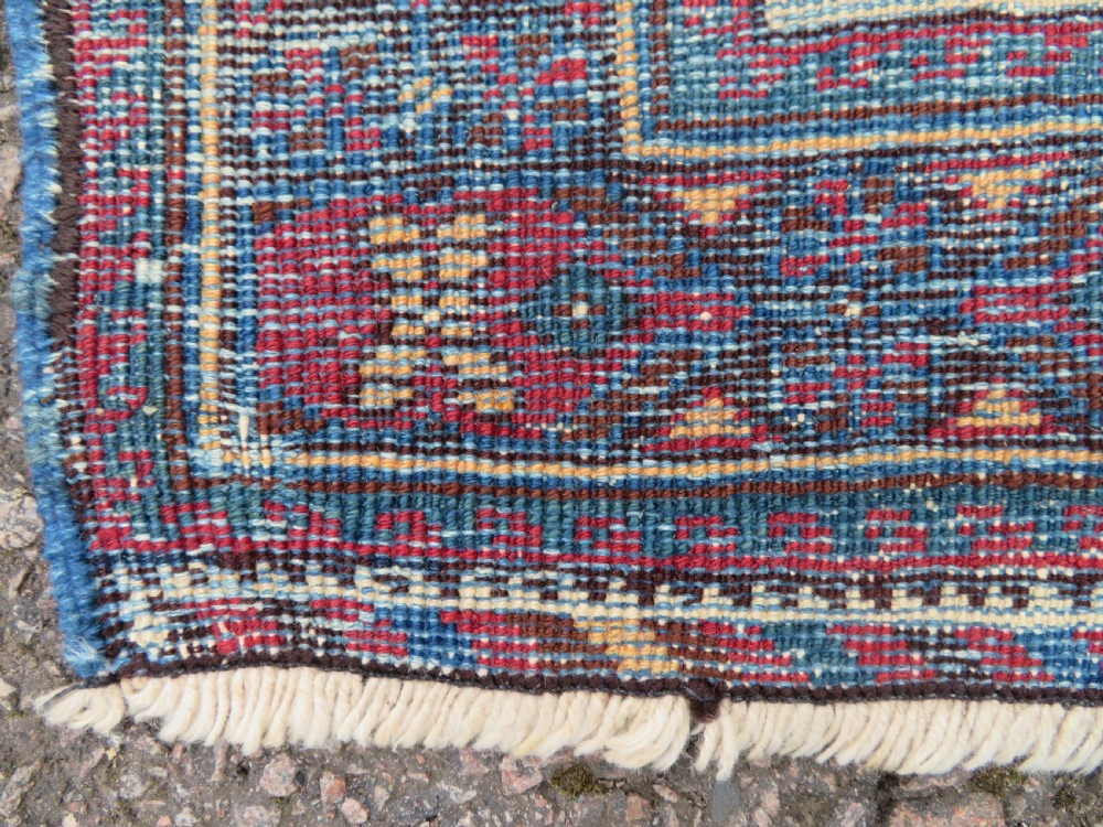 A hand-knotted antique Afshar tribal wool rug featuring a red stepped medallion on an indigo blue field surrounded by geometric borders. View X