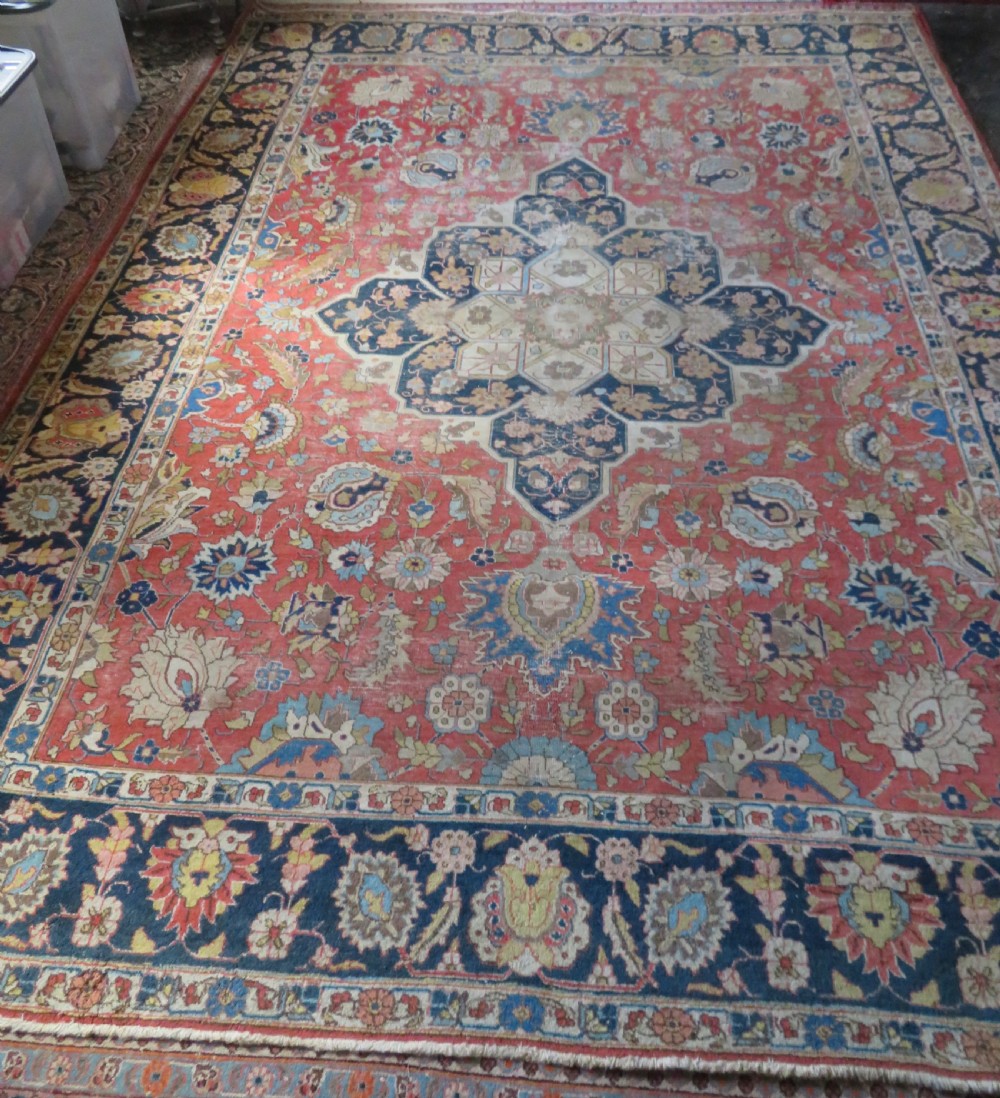 An antique hand-knotted Tabriz wool carpet featuring a central navy and cream medallion on a terracotta field with intricate floral borders.