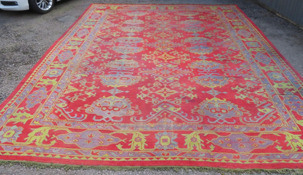 A large antique wool Ushak carpet featuring a coral red field decorated with light green and pastel medallion motifs and a patterned border.