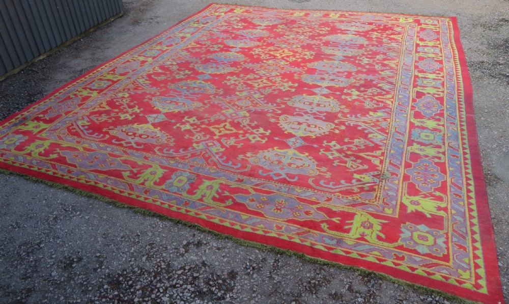 A large antique wool Ushak carpet featuring a coral red field decorated with light green and pastel medallion motifs and a patterned border. View II