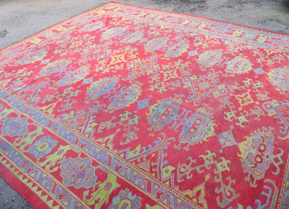A large antique wool Ushak carpet featuring a coral red field decorated with light green and pastel medallion motifs and a patterned border. View III