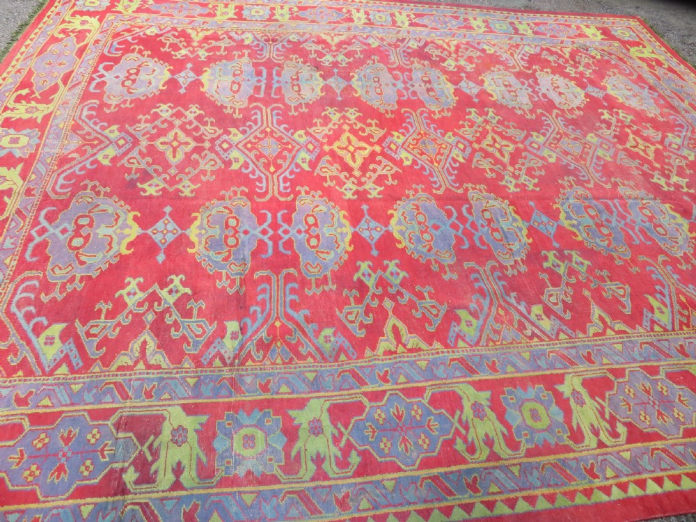 A large antique wool Ushak carpet featuring a coral red field decorated with light green and pastel medallion motifs and a patterned border. View IV