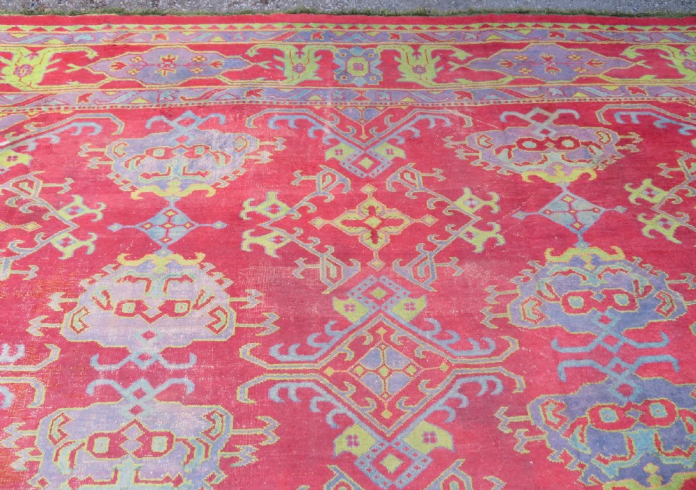 A large antique wool Ushak carpet featuring a coral red field decorated with light green and pastel medallion motifs and a patterned border. View VI