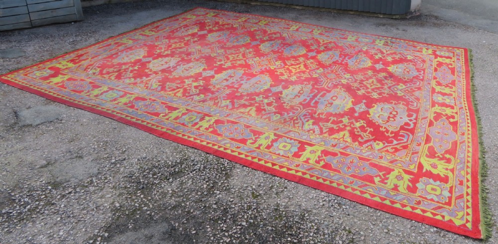 A large antique wool Ushak carpet featuring a coral red field decorated with light green and pastel medallion motifs and a patterned border. View VII