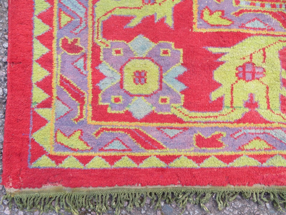 A large antique wool Ushak carpet featuring a coral red field decorated with light green and pastel medallion motifs and a patterned border. View IX
