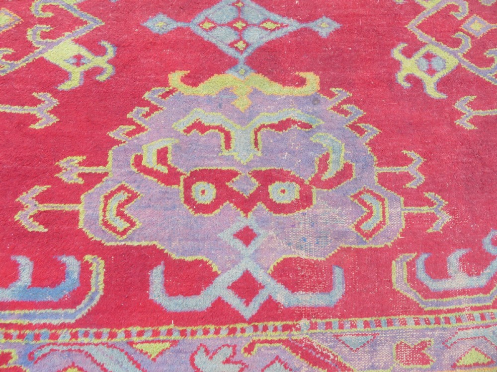 A large antique wool Ushak carpet featuring a coral red field decorated with light green and pastel medallion motifs and a patterned border. View X