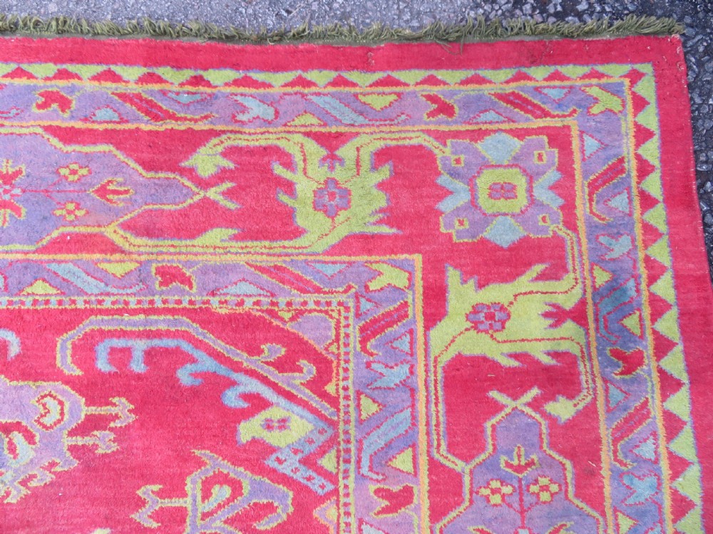 A large antique wool Ushak carpet featuring a coral red field decorated with light green and pastel medallion motifs and a patterned border. View XII