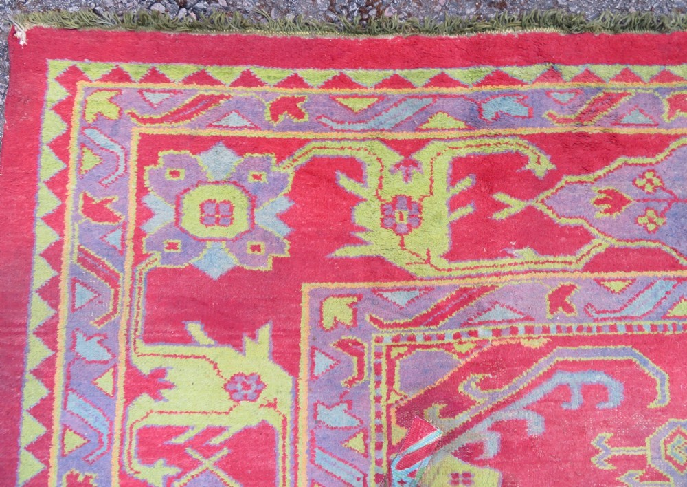 A large antique wool Ushak carpet featuring a coral red field decorated with light green and pastel medallion motifs and a patterned border. View XIII