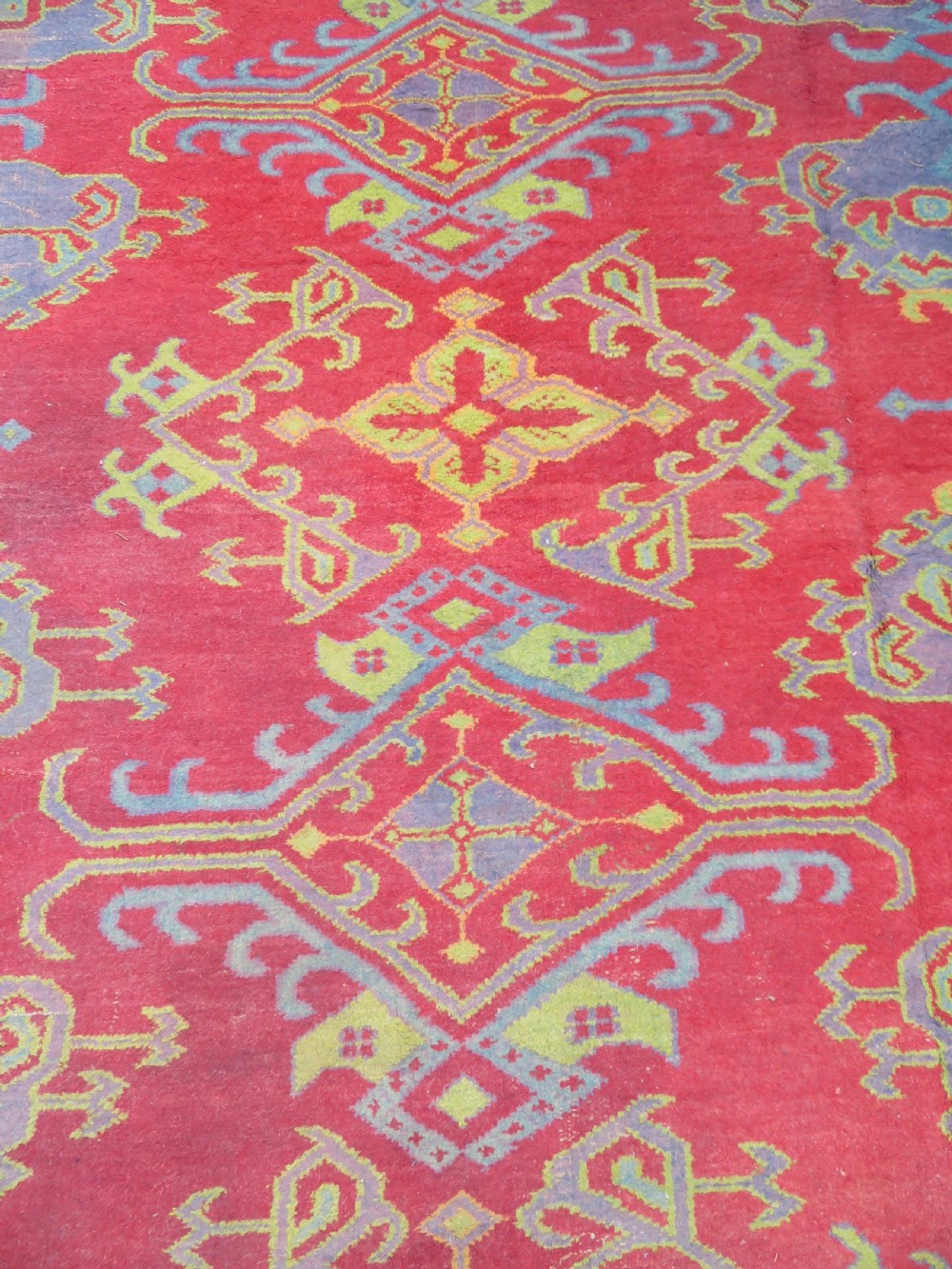 A large antique wool Ushak carpet featuring a coral red field decorated with light green and pastel medallion motifs and a patterned border. View XV