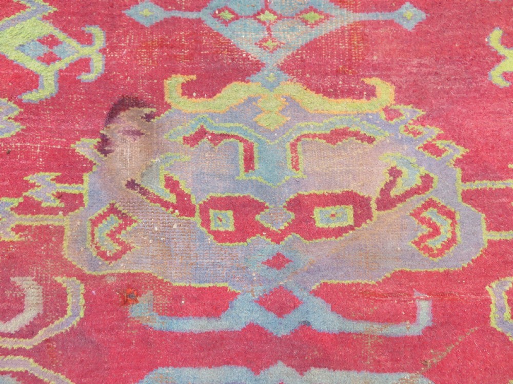 A large antique wool Ushak carpet featuring a coral red field decorated with light green and pastel medallion motifs and a patterned border. View XVI