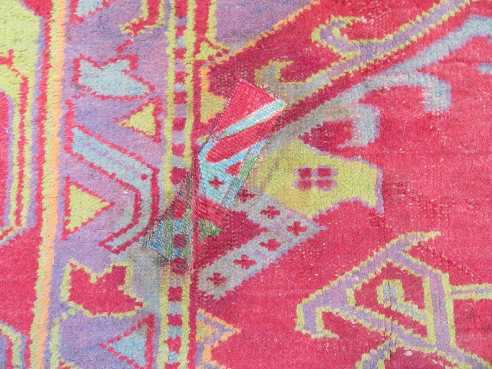 A large antique wool Ushak carpet featuring a coral red field decorated with light green and pastel medallion motifs and a patterned border. View XIX