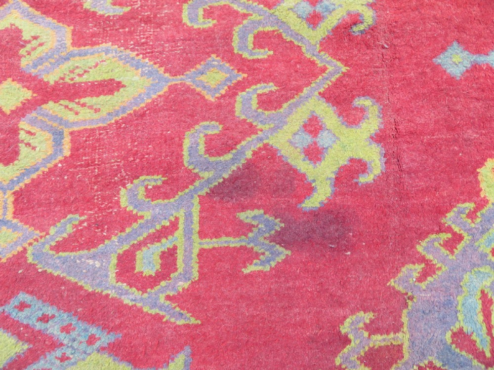 A large antique wool Ushak carpet featuring a coral red field decorated with light green and pastel medallion motifs and a patterned border. View XXI