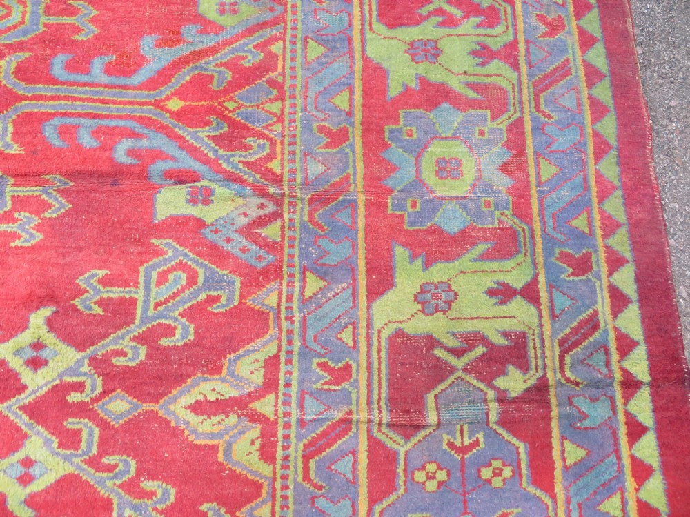 A large antique wool Ushak carpet featuring a coral red field decorated with light green and pastel medallion motifs and a patterned border. View XXII