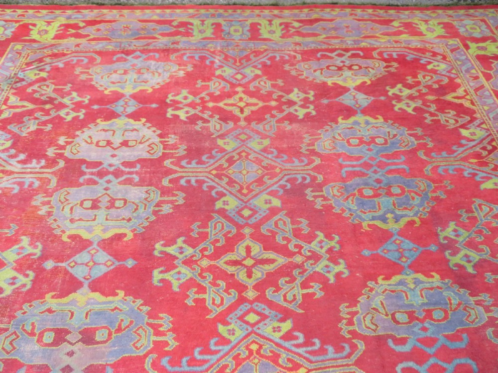 A large antique wool Ushak carpet featuring a coral red field decorated with light green and pastel medallion motifs and a patterned border. View XXV