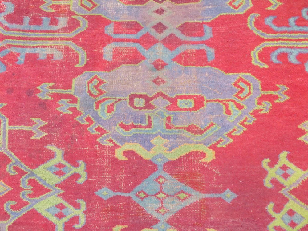 A large antique wool Ushak carpet featuring a coral red field decorated with light green and pastel medallion motifs and a patterned border. View XXVIII