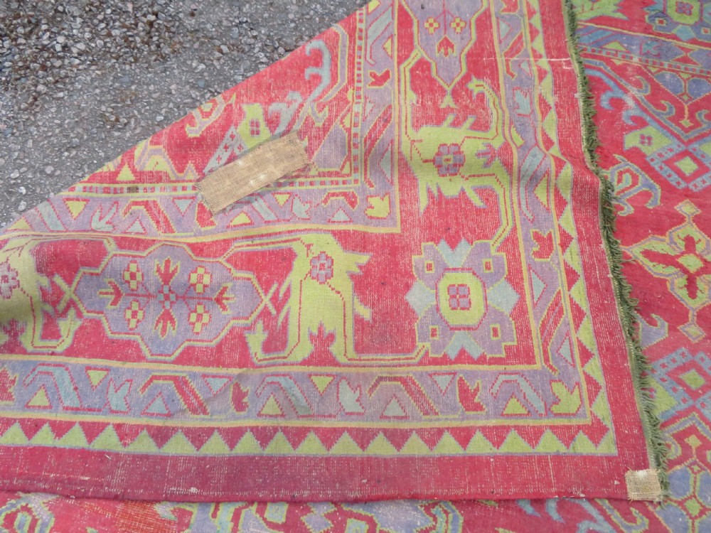 A large antique wool Ushak carpet featuring a coral red field decorated with light green and pastel medallion motifs and a patterned border. View XXIX