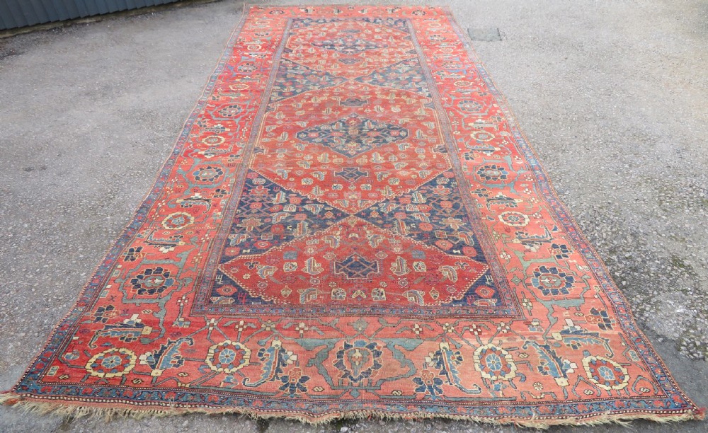 An antique Kurdish Bidjar Kelleh hand-knotted carpet featuring geometric diamond medallions on a terracotta red field with dark navy blue borders. View II