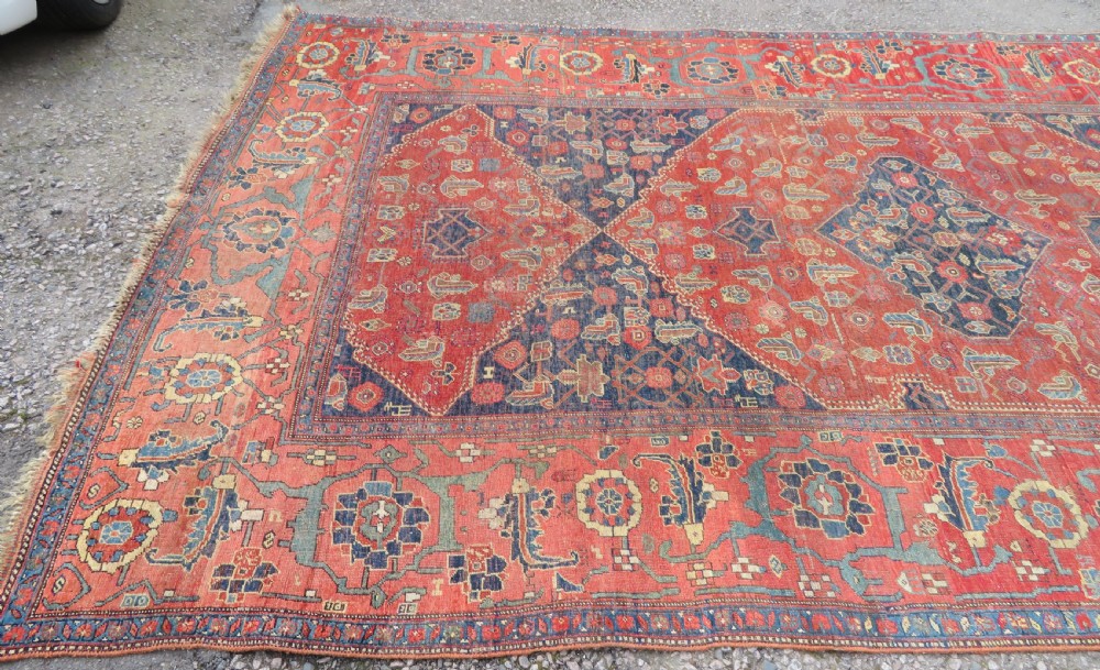 An antique Kurdish Bidjar Kelleh hand-knotted carpet featuring geometric diamond medallions on a terracotta red field with dark navy blue borders. View III