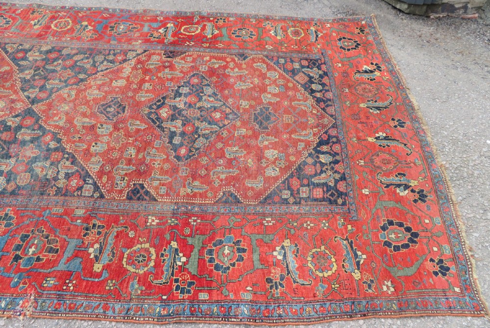 An antique Kurdish Bidjar Kelleh hand-knotted carpet featuring geometric diamond medallions on a terracotta red field with dark navy blue borders. View IV