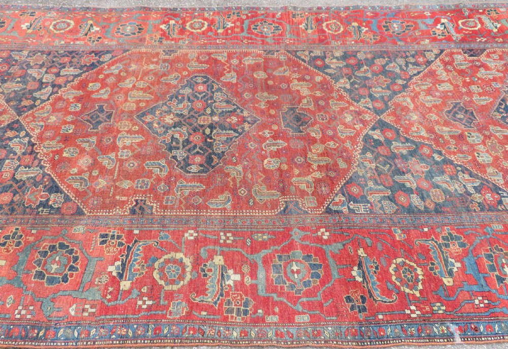 An antique Kurdish Bidjar Kelleh hand-knotted carpet featuring geometric diamond medallions on a terracotta red field with dark navy blue borders. View V