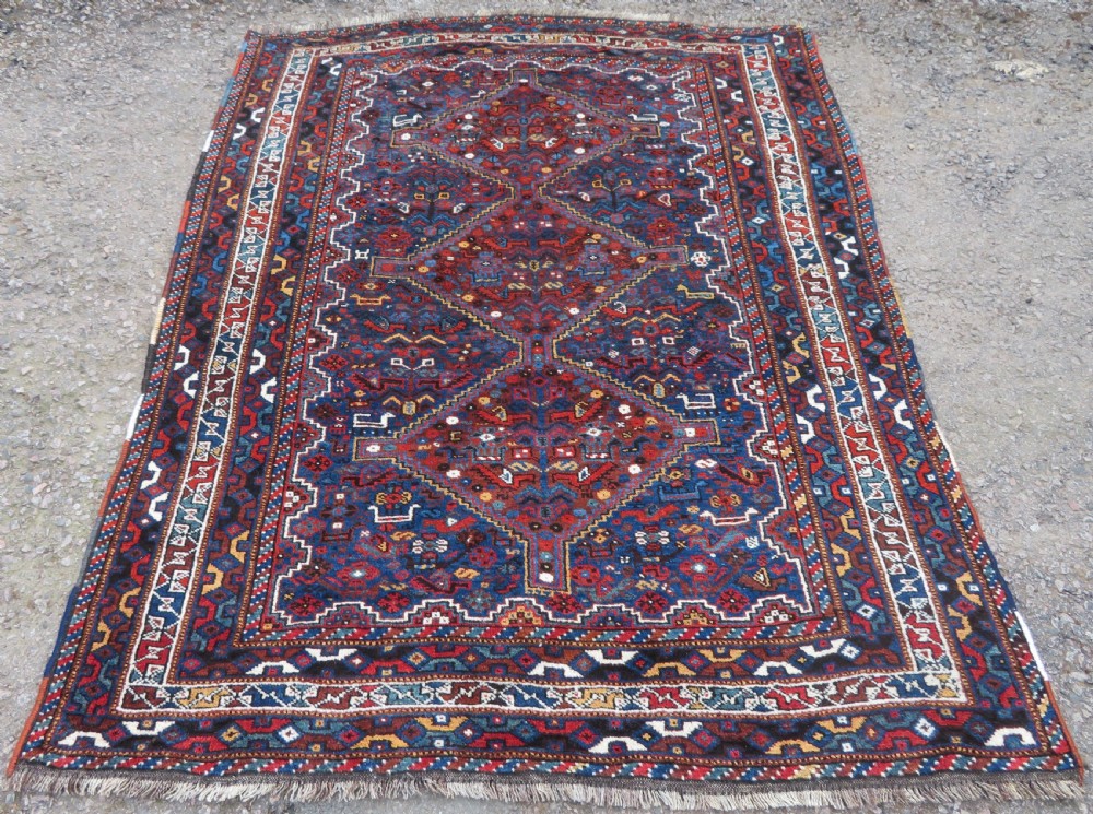 An antique Khamseh hand-knotted wool tribal rug featuring three central diamond medallions surrounded by small bird and geometric motifs in deep blue, terracotta red, and cream.